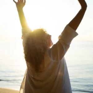 Mujer levantando las manos al sol en la playa con sensación de libertad Limbo - Grupos de Apoyo