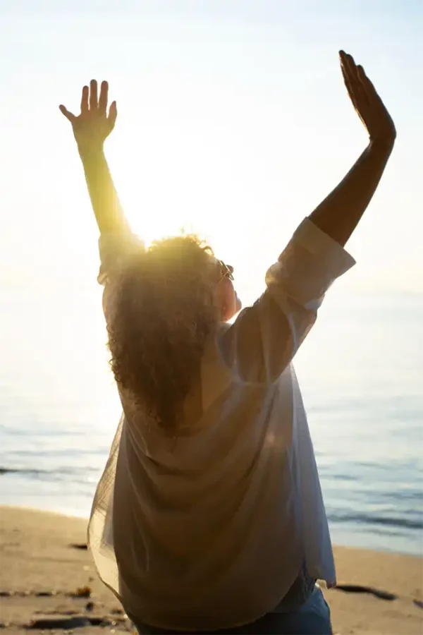 Mujer levantando las manos al sol en la playa con sensación de libertad Limbo - Grupos de Apoyo